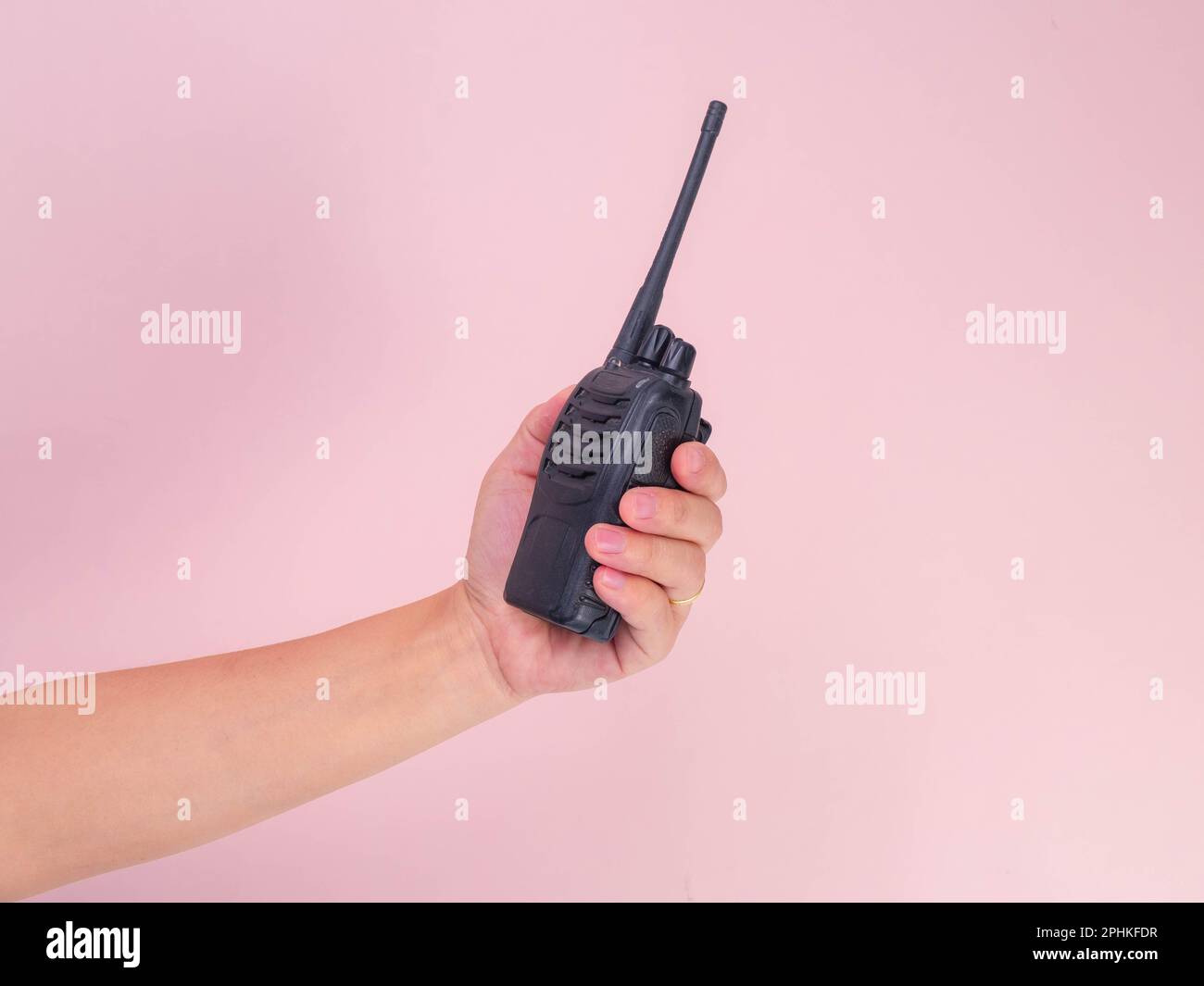 Close up hand holding portable walkie talkie isolated on pink background. Black handheld walkie talkie Stock Photo