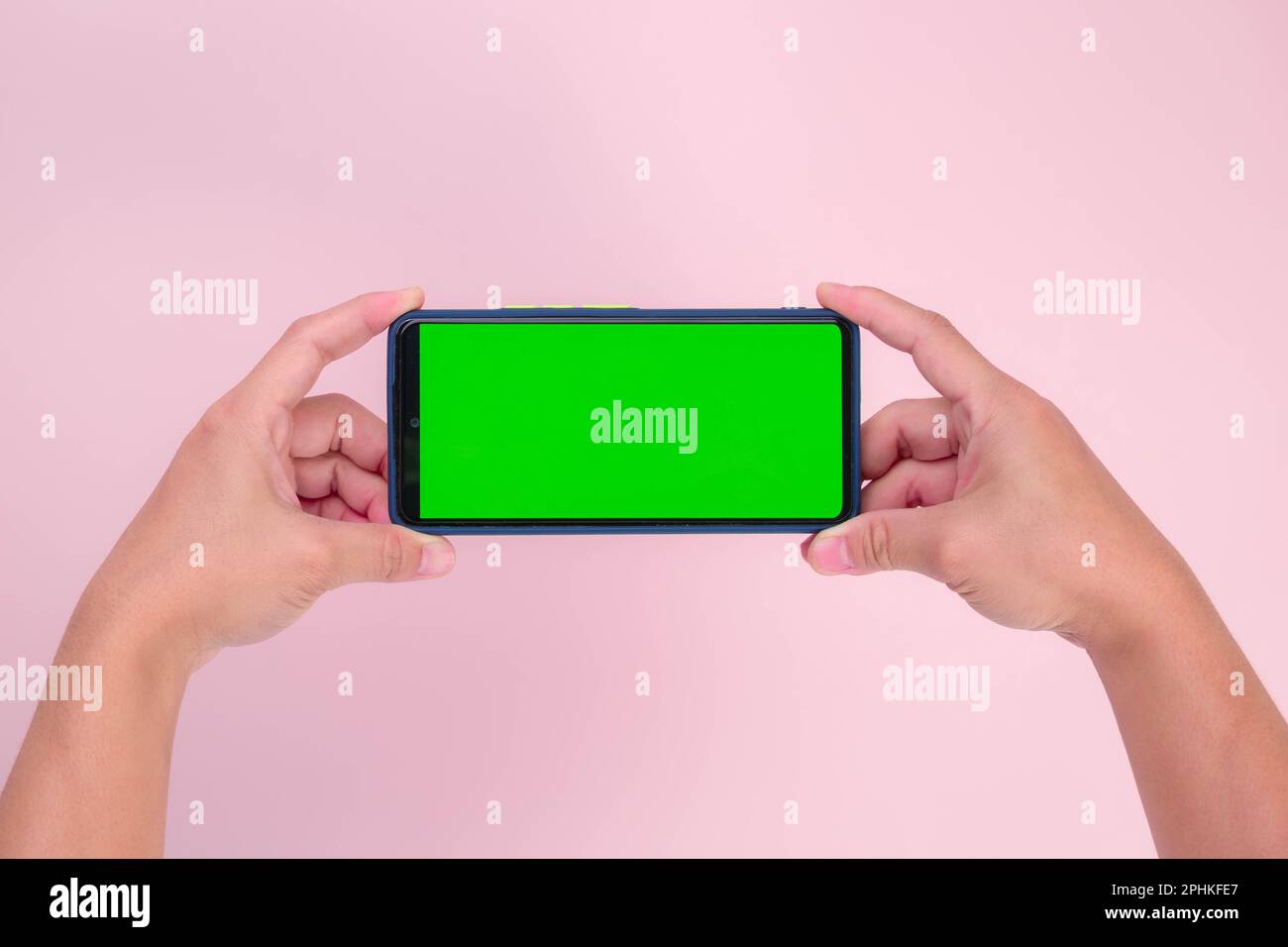 Human hand holding mobile smartphone with green screen in horizontal position isolated on pink background. clipping path Stock Photo