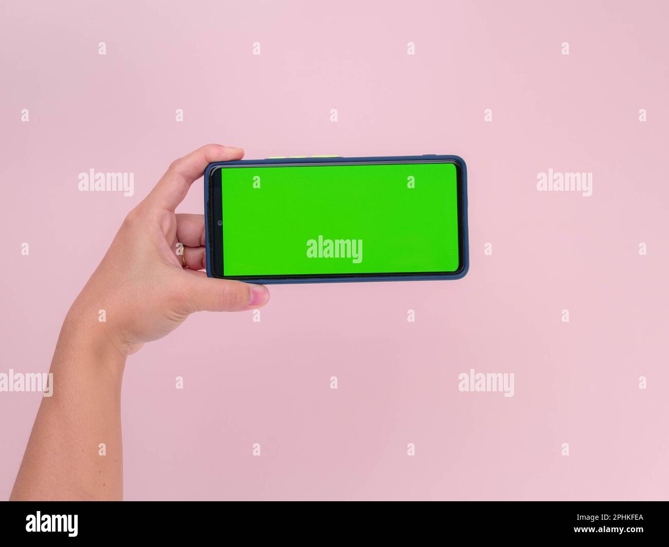 Human hand holding mobile smartphone with green screen in horizontal position isolated on pink background. clipping path Stock Photo