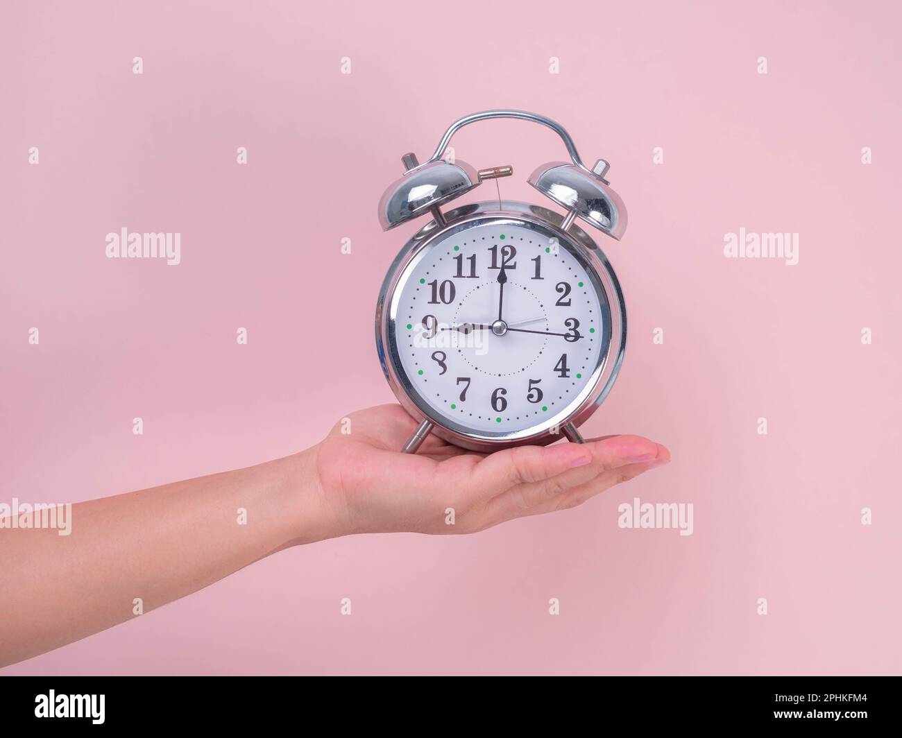 Female hand holding classic alarm clock on pink background. Close up of alarm clock in hand. Stock Photo