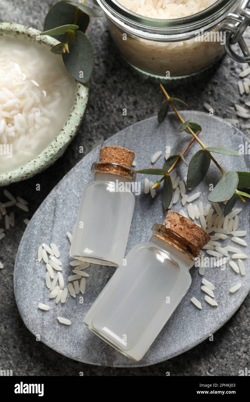 Glass bottles with rice water and soaked grains on grey table, above ...