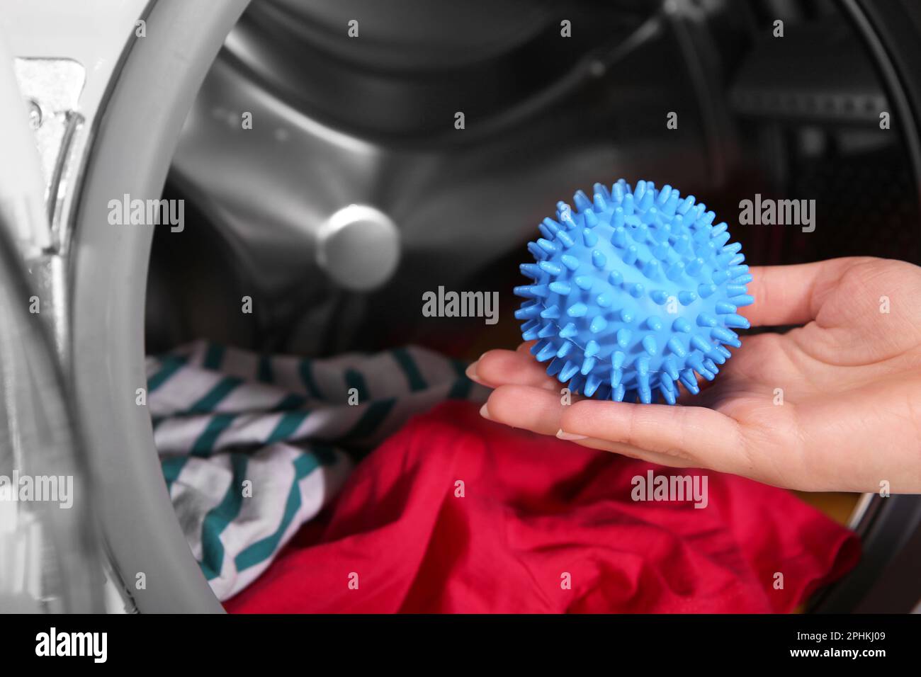 Woman putting blue dryer ball into washing machine, closeup Stock Photo