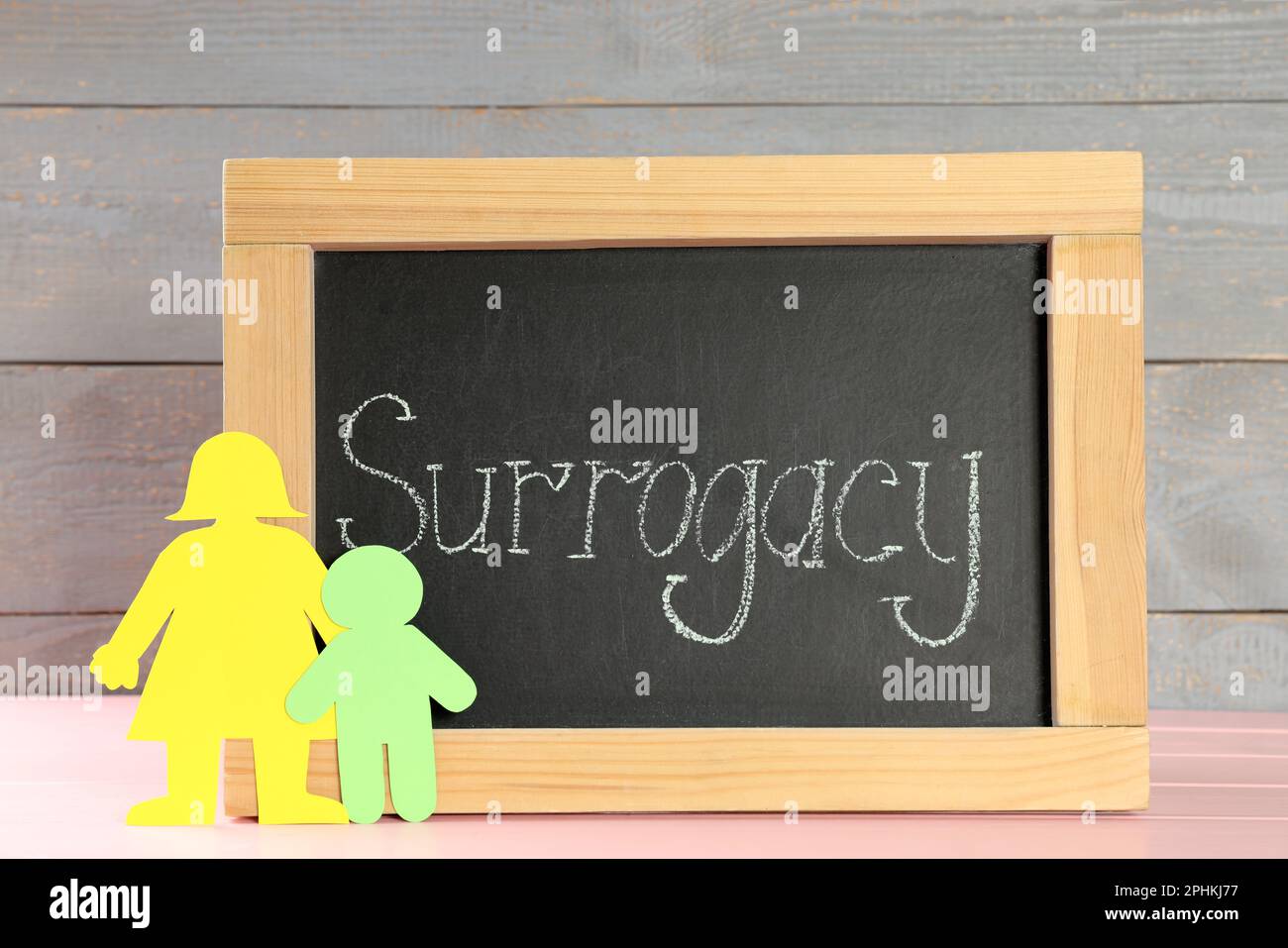 Small chalkboard with word Surrogacy and paper people cutouts on pink wooden table Stock Photo