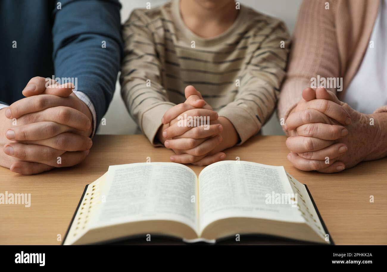 Boy and his godparents praying together at wooden table, closeup Stock Photo