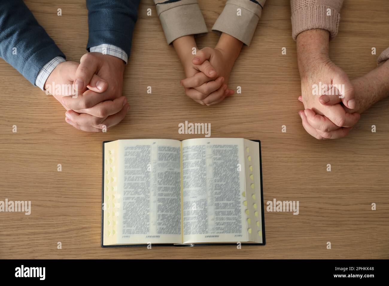 Boy and his godparents praying together at wooden table, top view Stock Photo