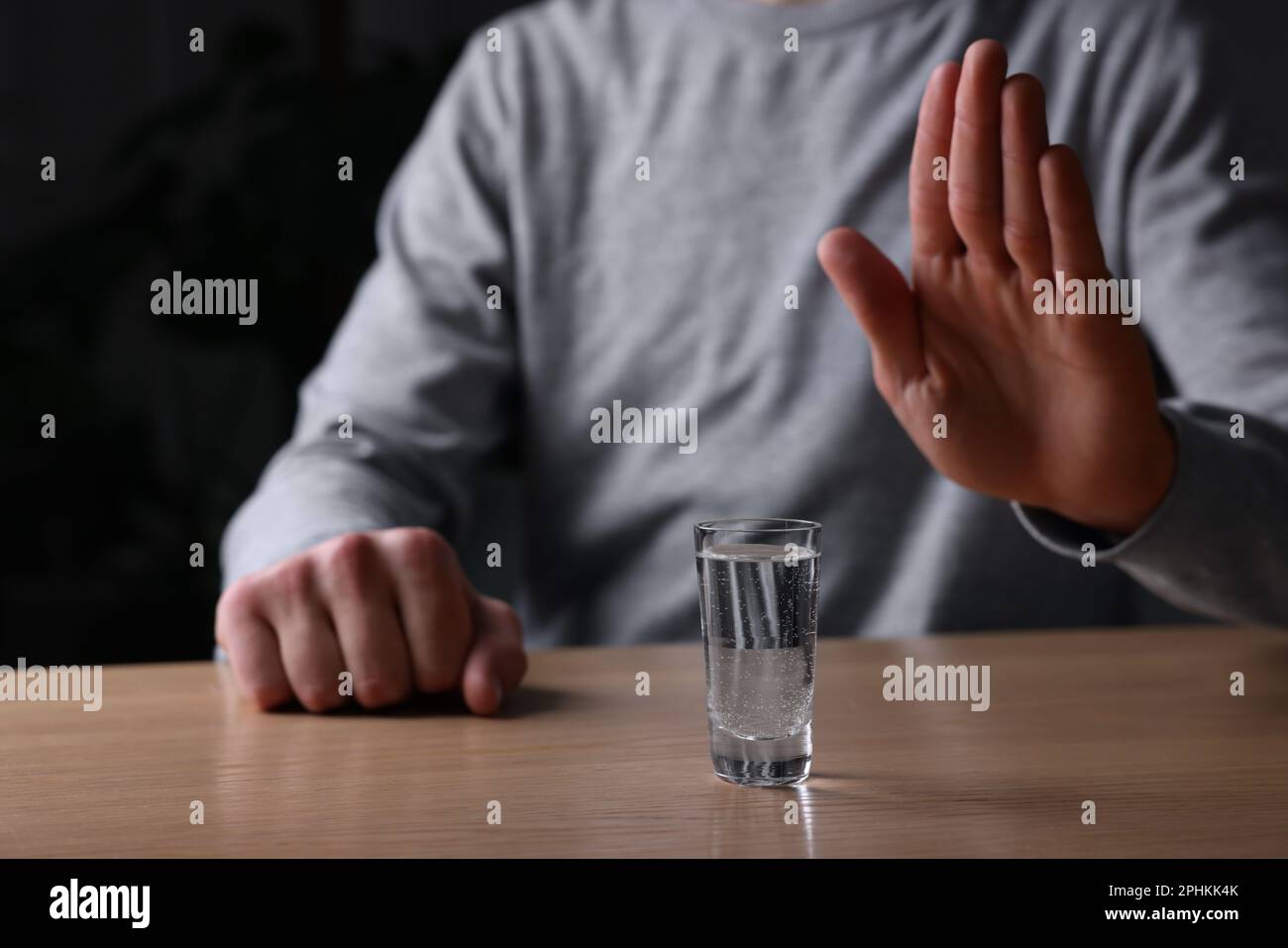 Man refusing to drink vodka at wooden table, closeup. Alcohol addiction