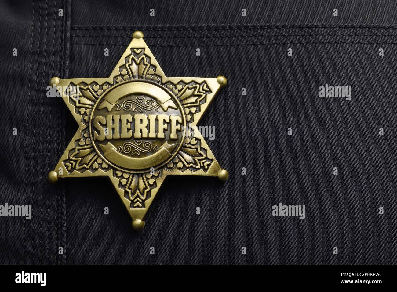 A gold coloured metal Sheriff badge in the shape of a six pointed star on a black jacket Stock Photo