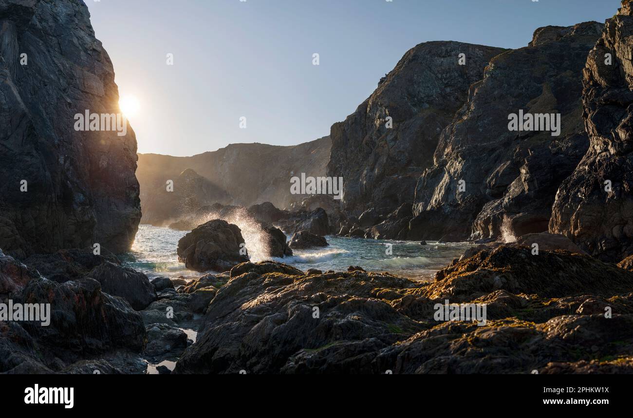 Waves crashing in at sunset onto the rocks of the far beach of Kynance Cove, on a summer day on the Lizard Peninsula in Cornward, England Stock Photo