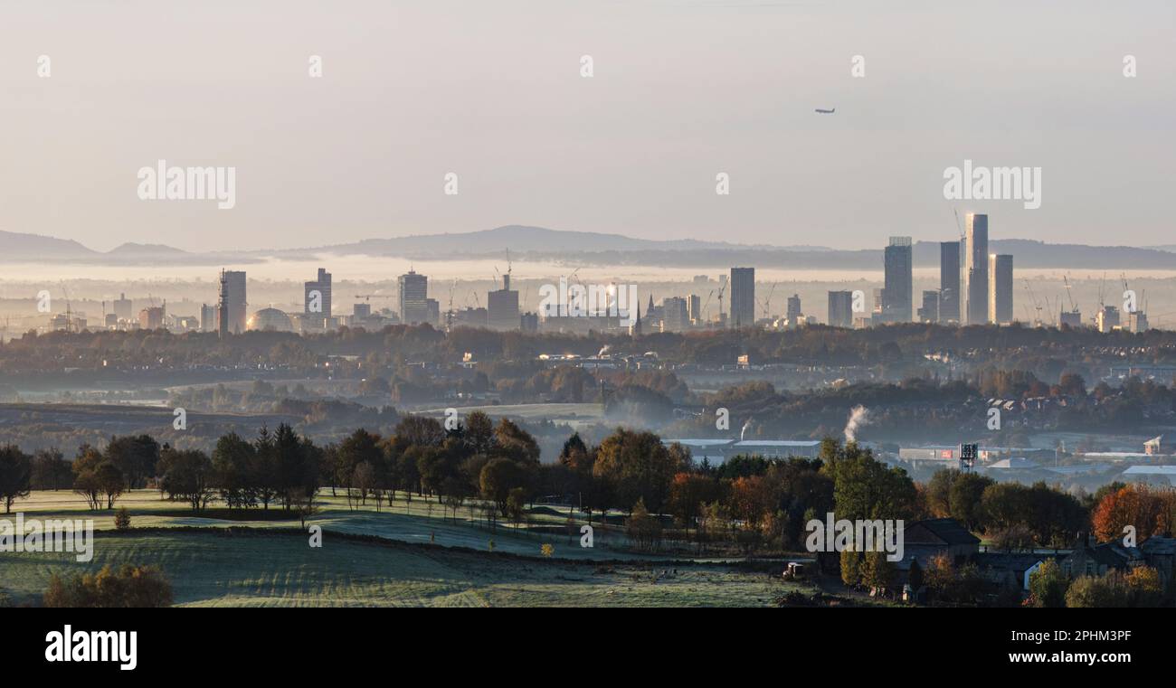 Distant towers of Manchester on a frosty winters morning with a bit of mist in the air with hills, trees, landscapes and countryside in the foreground Stock Photo
