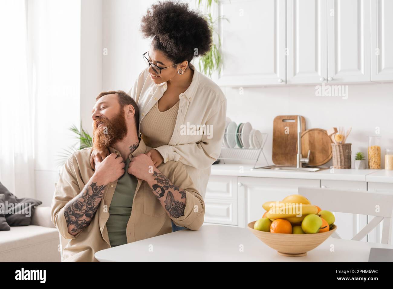 Positive african american woman hugging tattooed boyfriend in kitchen ...