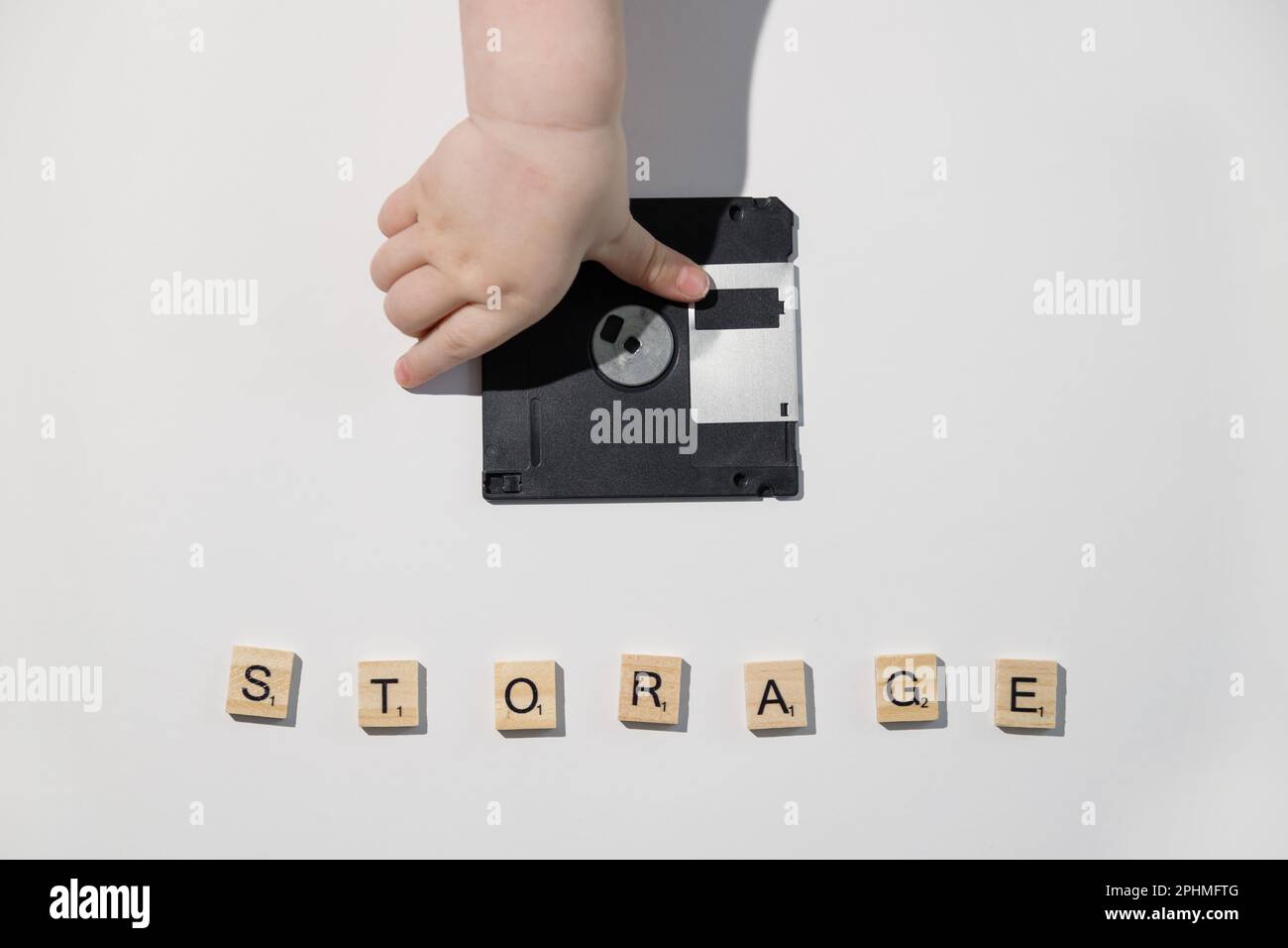 Child hand put floppy disk on white table. Backup and saving information concept. Memory Stock Photo