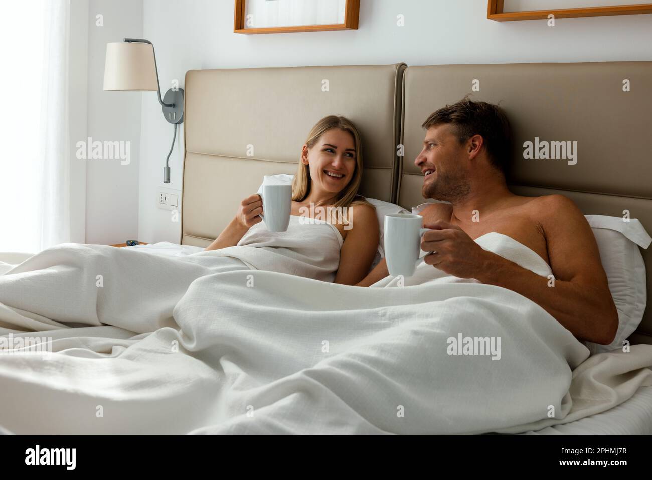 happy couple laying in bed and drinking morning coffee at home bedroom Stock Photo