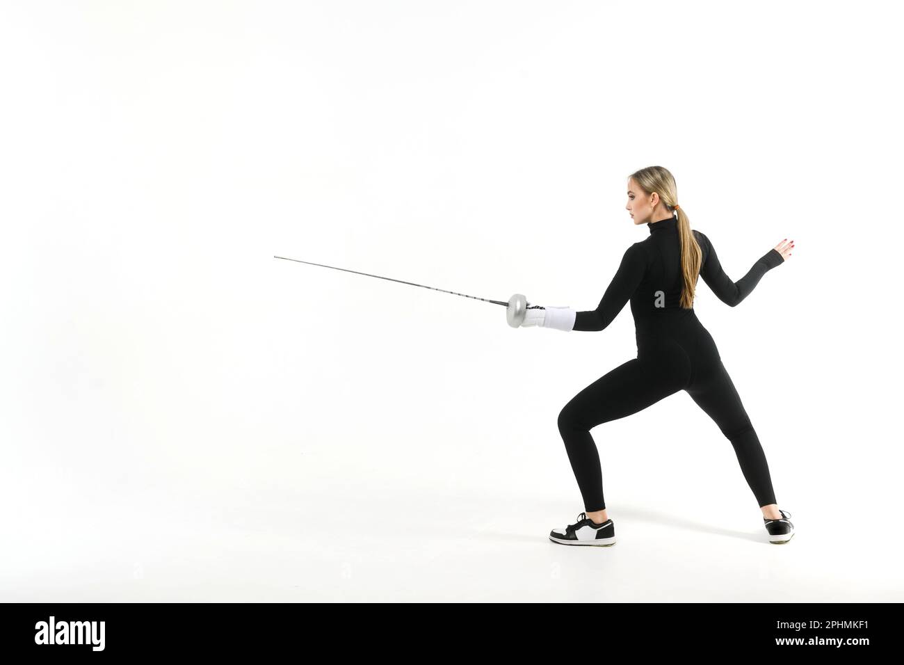 Teenage girl in a black tight-fitting jumpsuit practicing with a sword on a white background Stock Photo