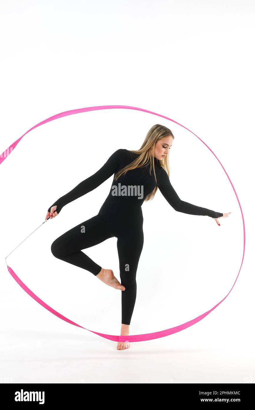 Girl gymnast in a black tight-fitting jumpsuit with a pink ribbon on a white background Stock Photo