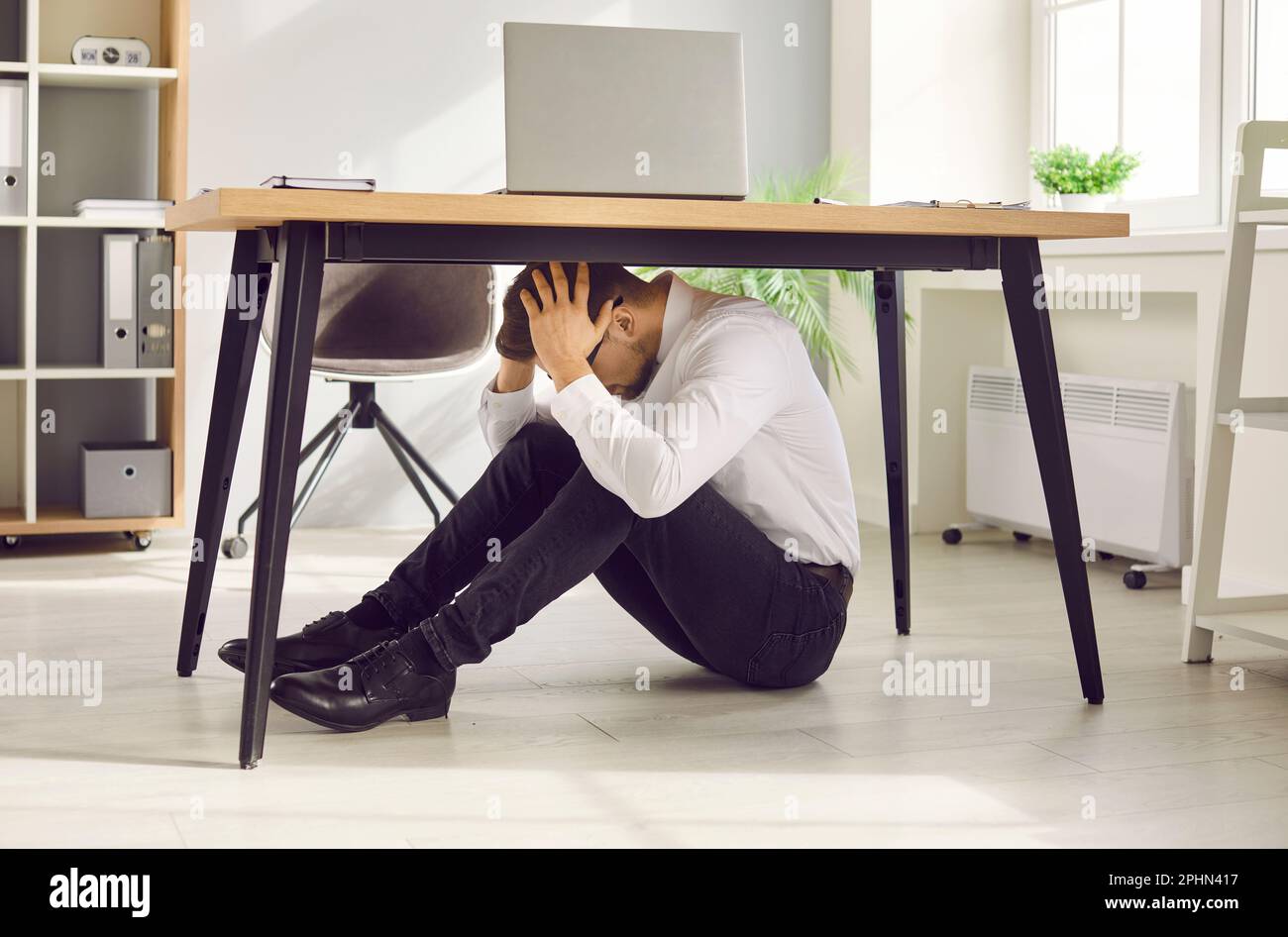 Scared office worker hiding under desk to protect himself during