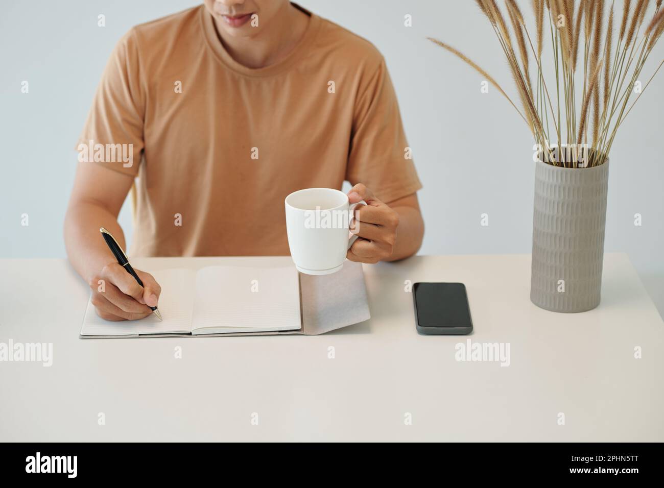 Man drinking morning coffee and writing in planner Stock Photo