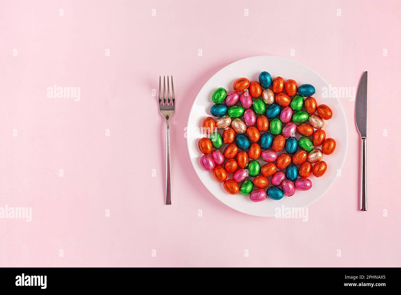 Happy Easter. Table setting for Easter holiday. Easter chocolate eggs and cutlery on pink background. Top view, flat lay Stock Photo