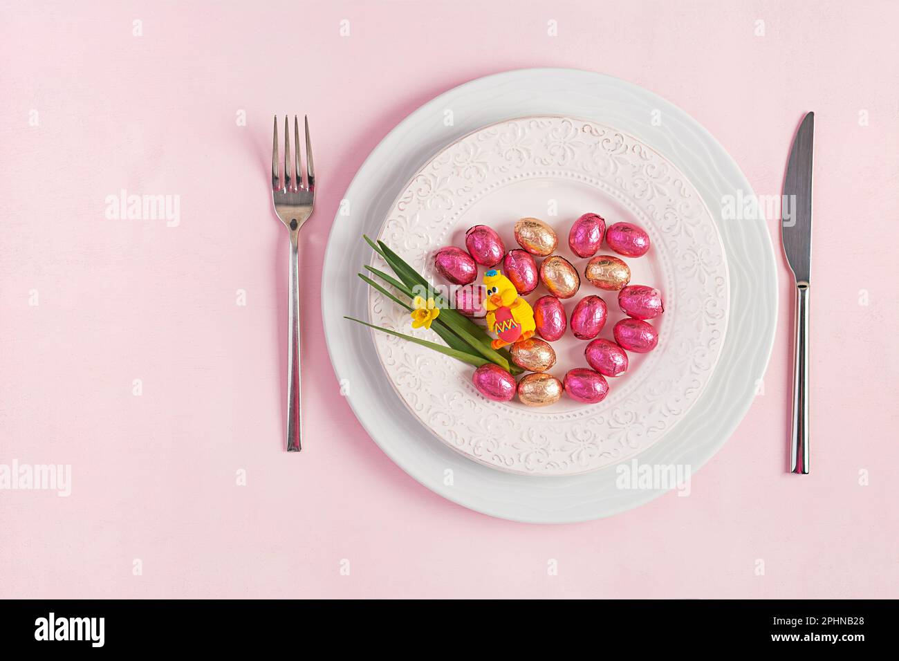 Happy Easter. Table setting for Easter holiday. Easter eggs, duck, flower and cutlery on pink background. Top view, flat lay Stock Photo