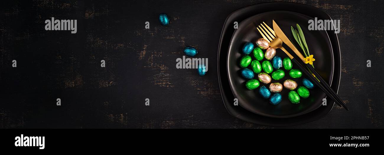 Happy Easter. Table setting for Easter holiday. Easter chocolate eggs and cutlery on dark background. Top view, banner Stock Photo
