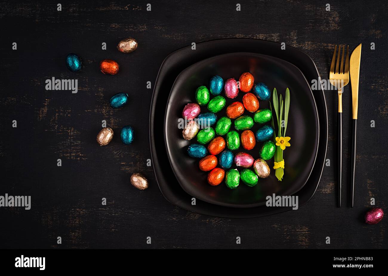Happy Easter. Table setting for Easter holiday. Easter chocolate eggs and cutlery on dark background. Top view, flat lay Stock Photo