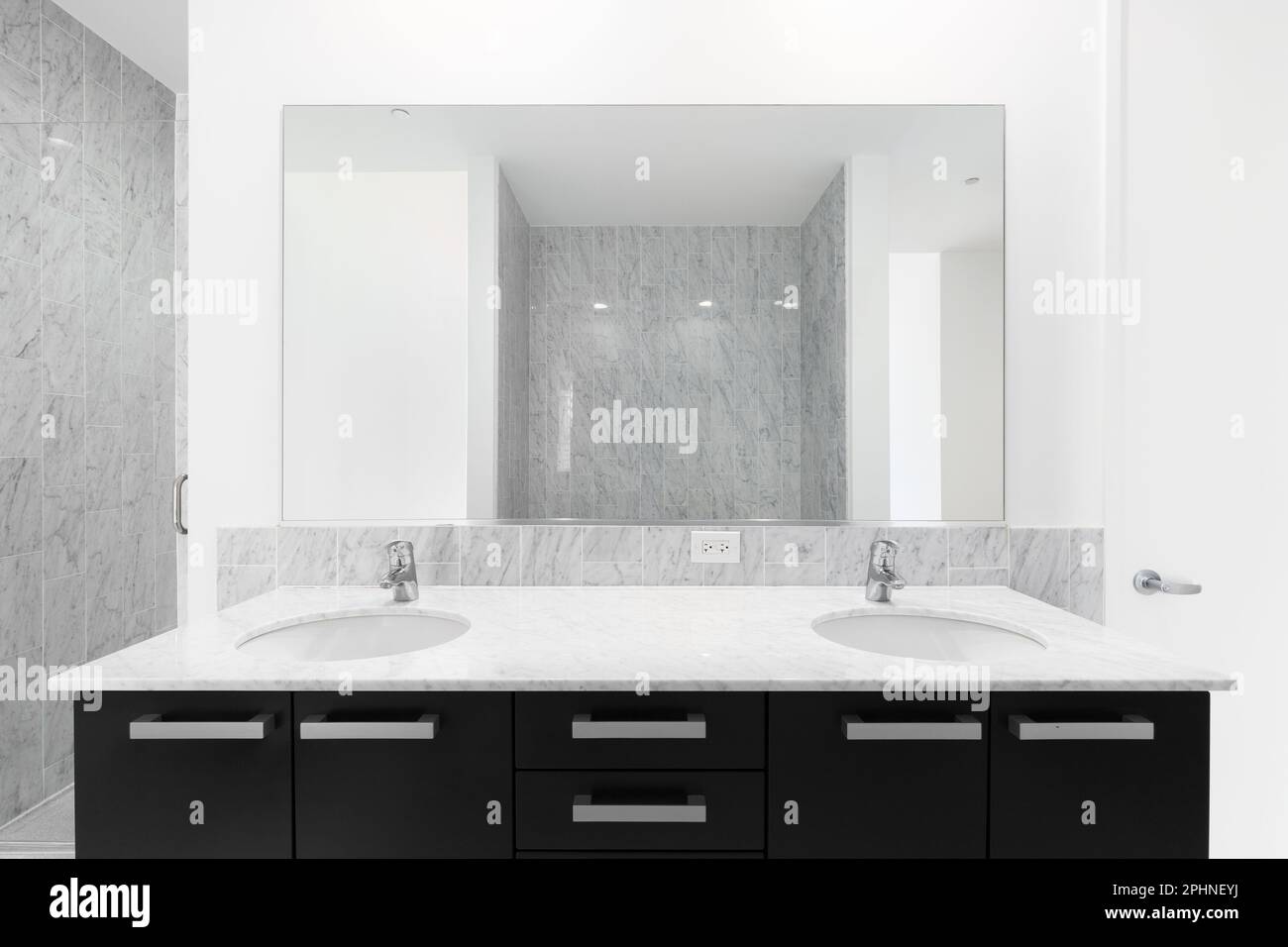 A modern bathroom with a black marble countertop, and two showers with marble subway