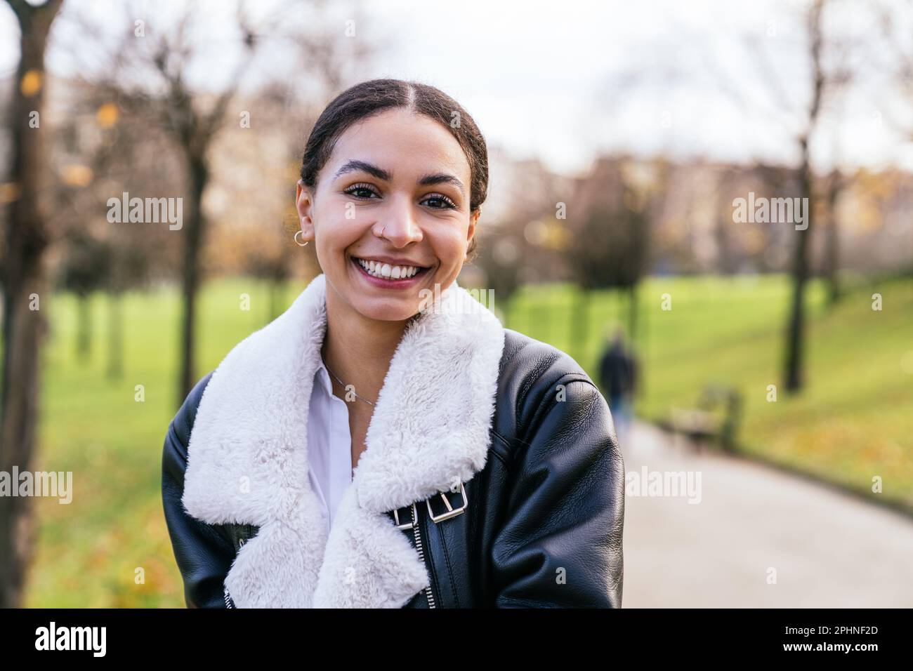 Caucasian beauty beaming in casual attire, posing at park with cityscape sunset view, radiating charm with a captivating smile. Stock Photo