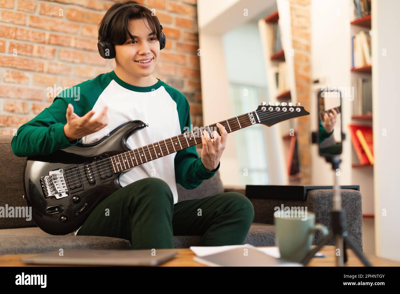 Aisan Guy Playing Electric Guitar In Front Of Phone Indoors