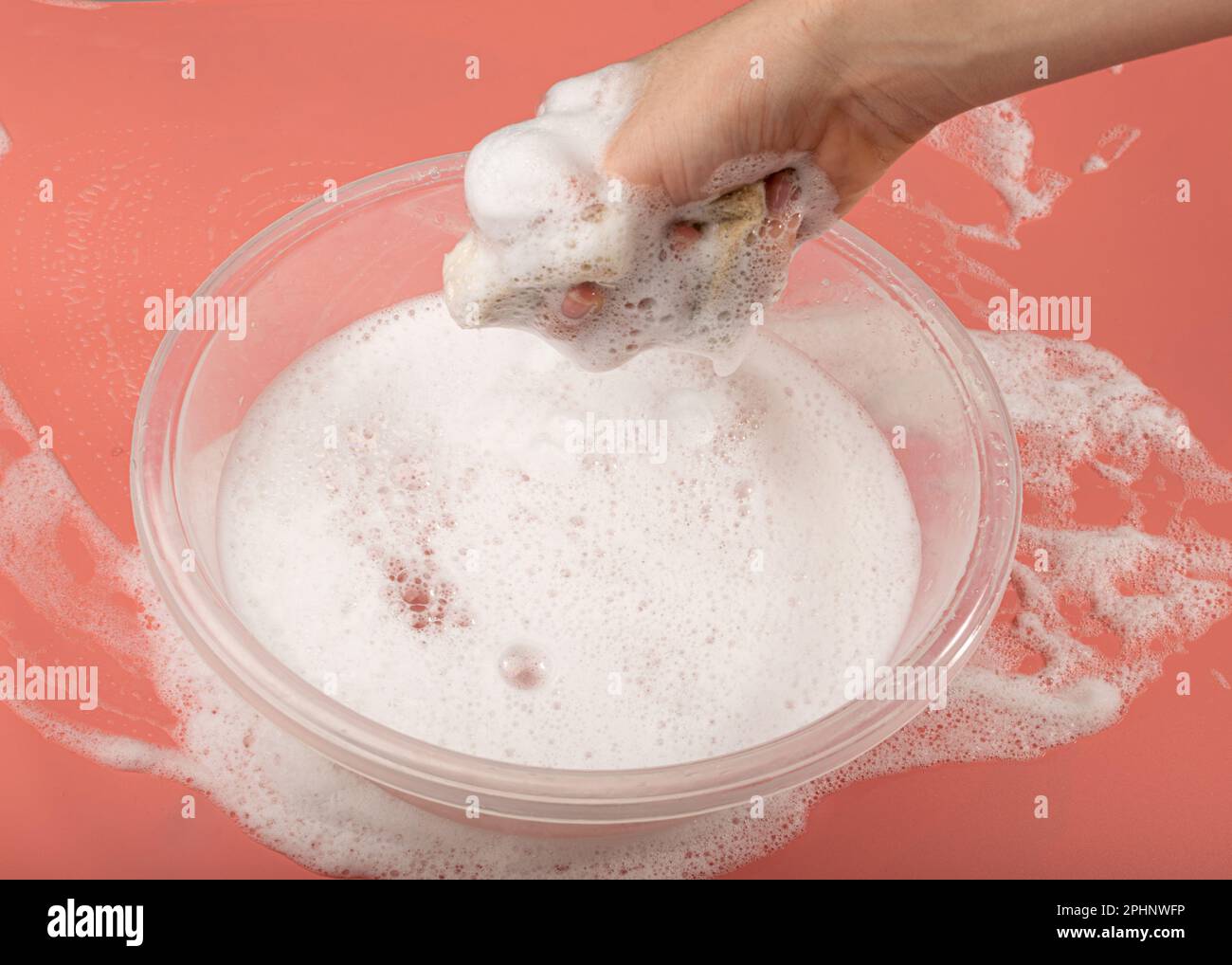 A Basin with Soapy Water, Hand Holds Soapy Sponge with Foam on Pink Background, Copy Space Stock Photo