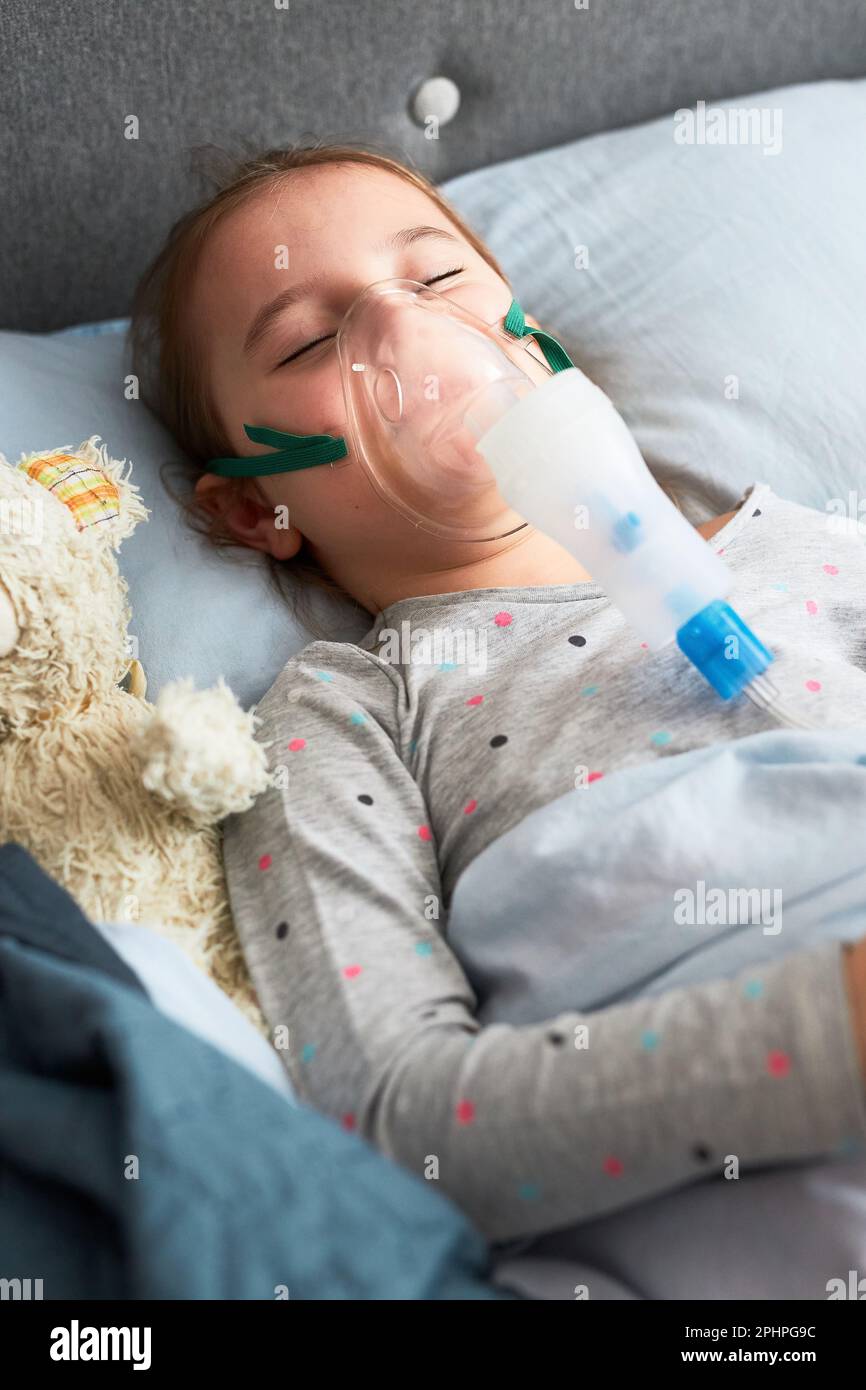 Sick little girl having medical inhalation treatment with nebuliser. Child with breathing mask on her face lying in bed Stock Photo