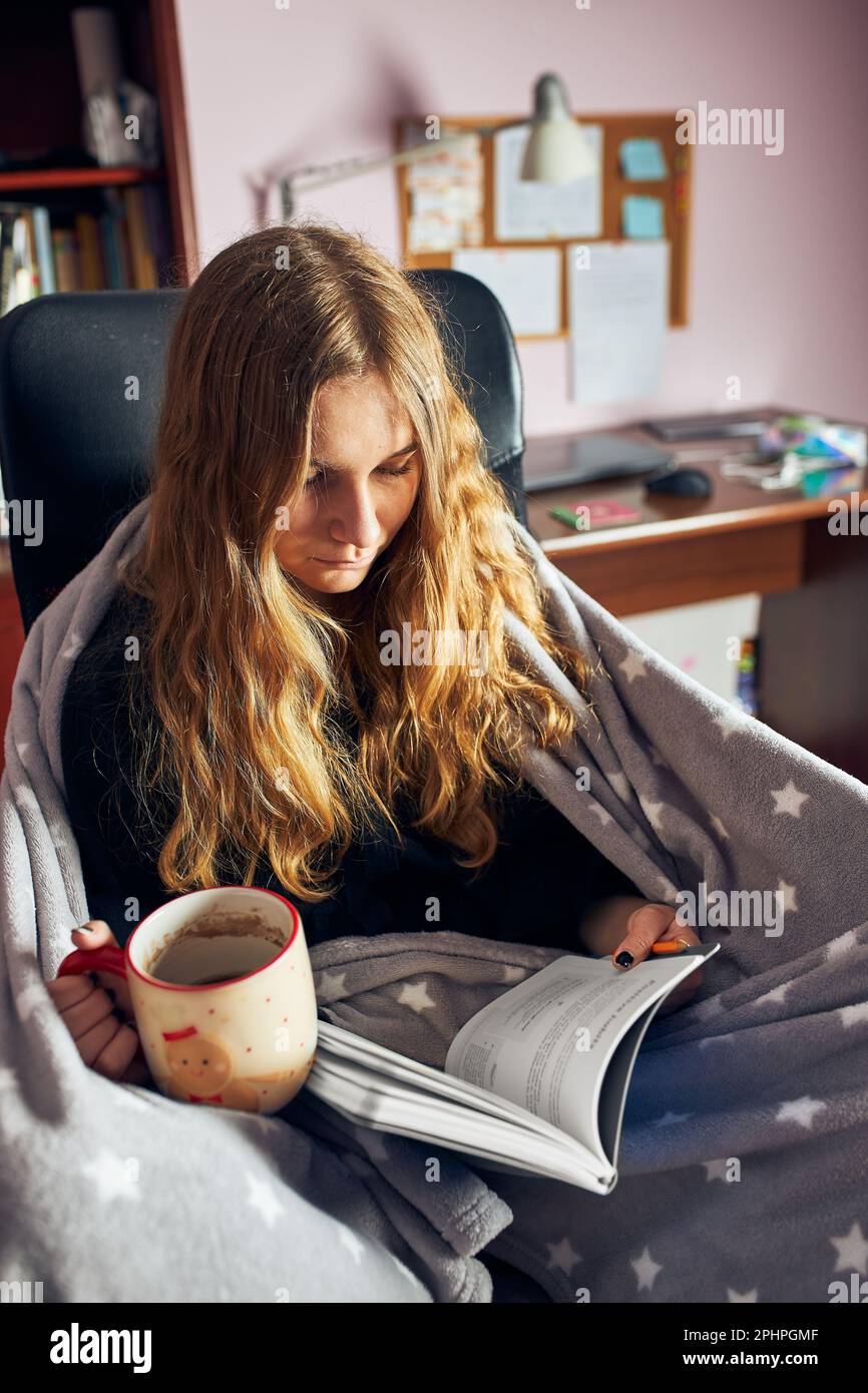 Student learning at home. Young woman making notes, reading and learning from notepad sitting in bed at home during quarantine Stock Photo