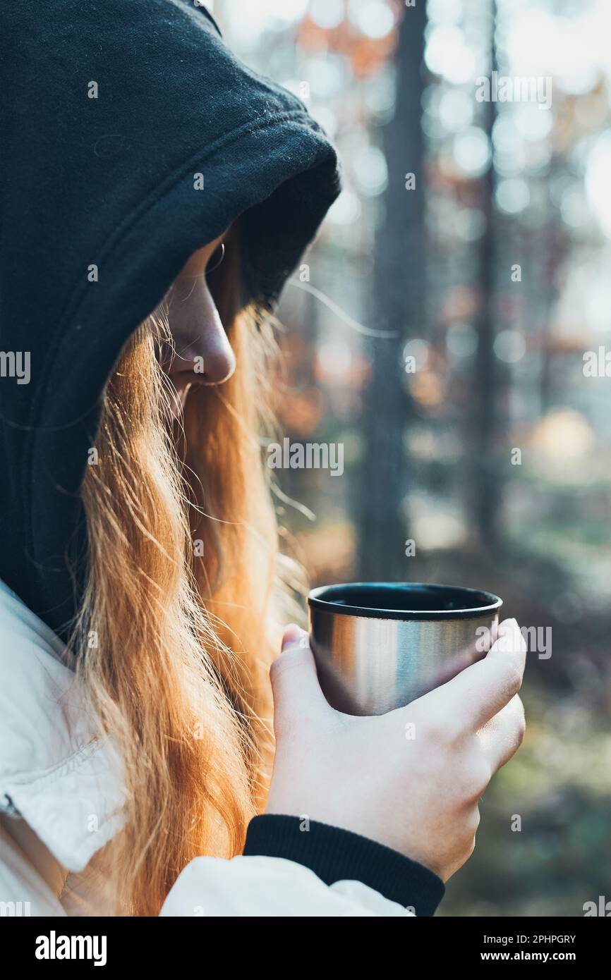 Woman holding metal cup. Thermos with hot drink on table