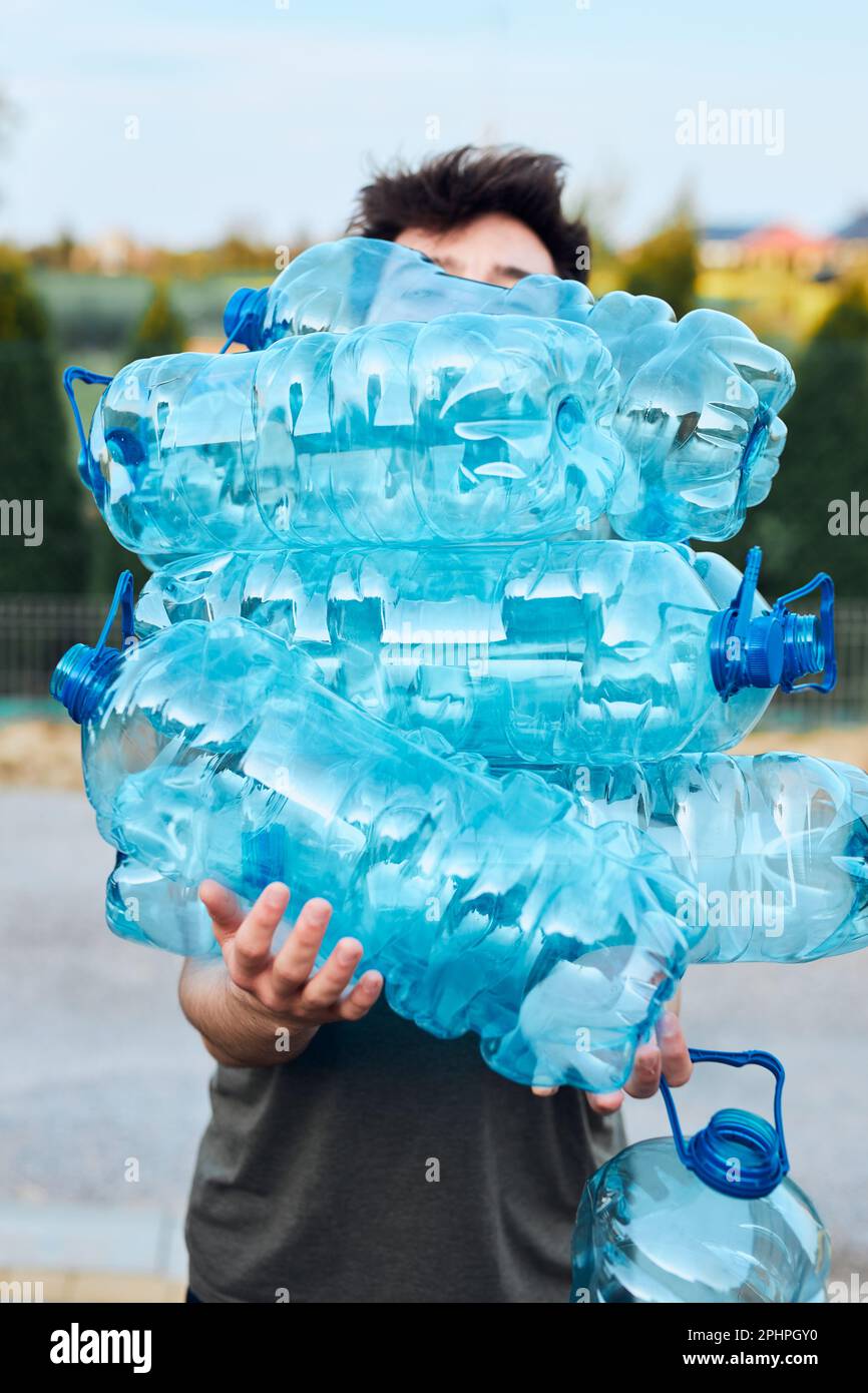 Young man throwing out empty used plastic water bottles into trash bin