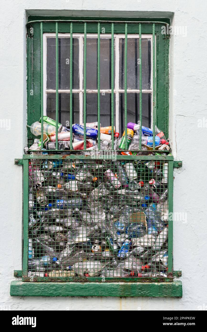 Lots of plastic bottles and cans dumped through metal bars and grille on a window of a commercial building. Stock Photo