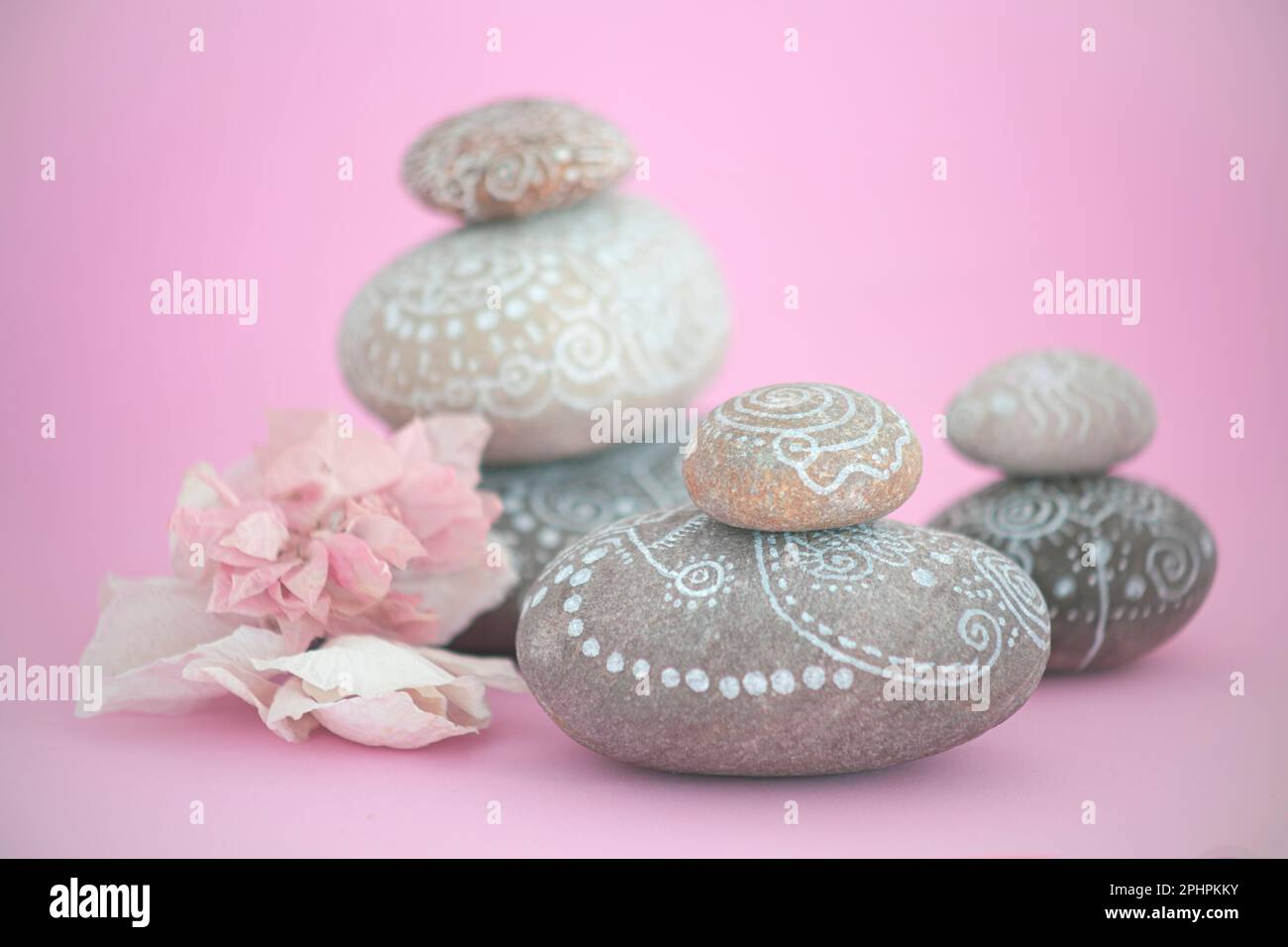 Zen style stacked stones with white line drawings about the universe. there is a pink flower next to the stones on a pink background that transmits ca Stock Photo