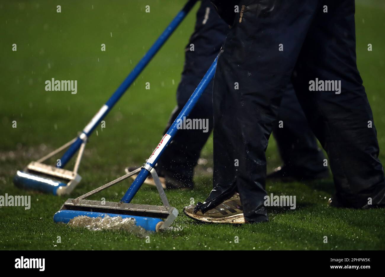 Members of ground staff attempt to sweep water from the pitch ahead of the Sky Bet League One match at the Completely-Suzuki Stadium, Cheltenham. Picture date: Wednesday March 29, 2023. Stock Photo