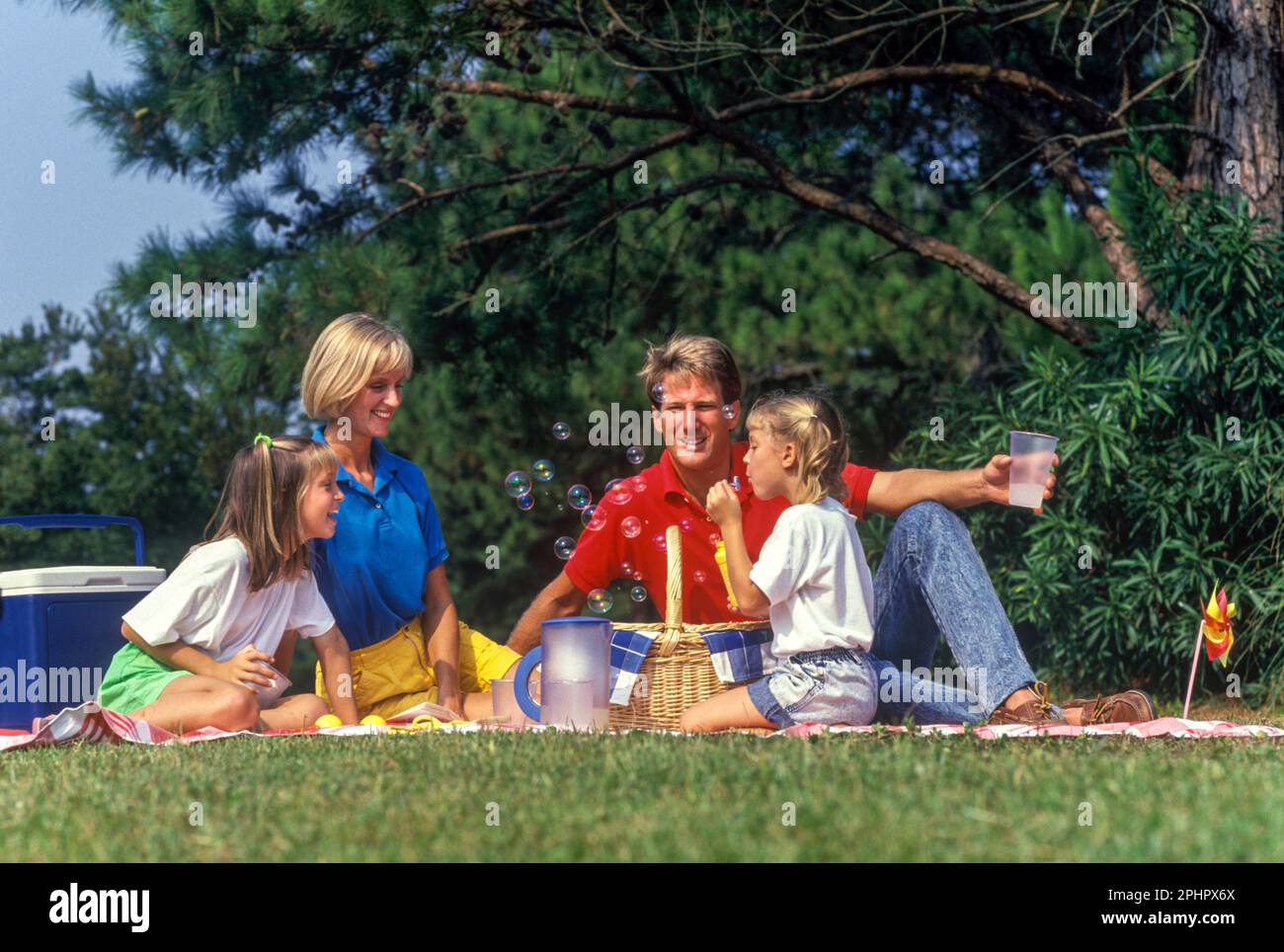 1990 HISTORICAL FAMILY SITTING TOGETHER ON BLANKET OUTSIDE ON PICNIC Stock Photo