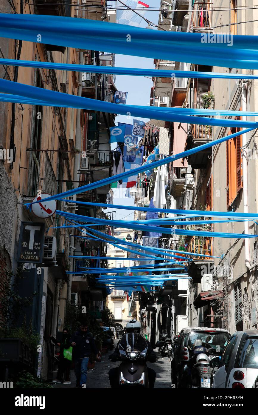 Naples, Italy. 22nd Mar, 2023. A man on a scooter passes next to banners and ribbons with the colors of the SSC Napoli soccer team in downtown. Preparations are in full swing in the city to celebrate the final victory of SSC Napoli, which leads the Italian championship with a 19-point lead with 11 games to go. Credit: Independent Photo Agency/Alamy Live News Stock Photo
