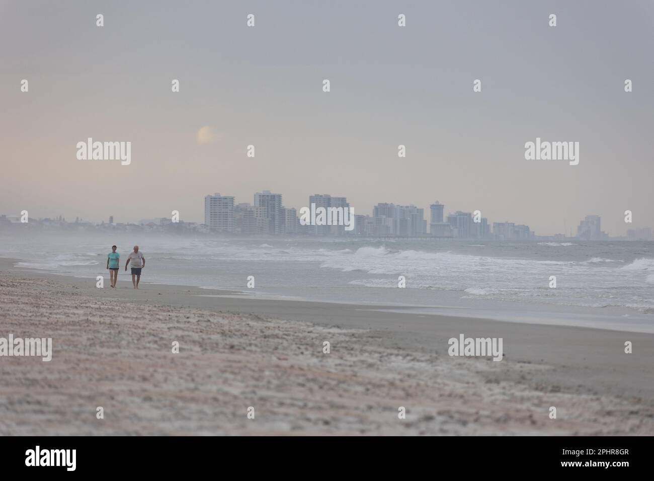 old-couple-walking-on-the-beach-during-sunset-with-new-smyrna-beach-in
