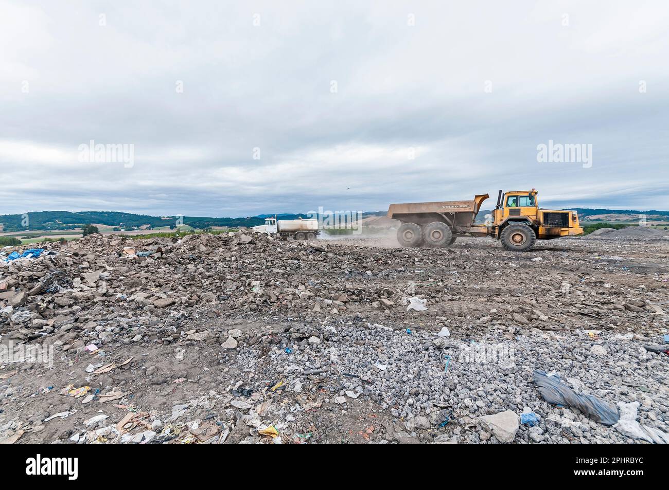 A dump truck kicking up dust, and a water truck watering down the dust