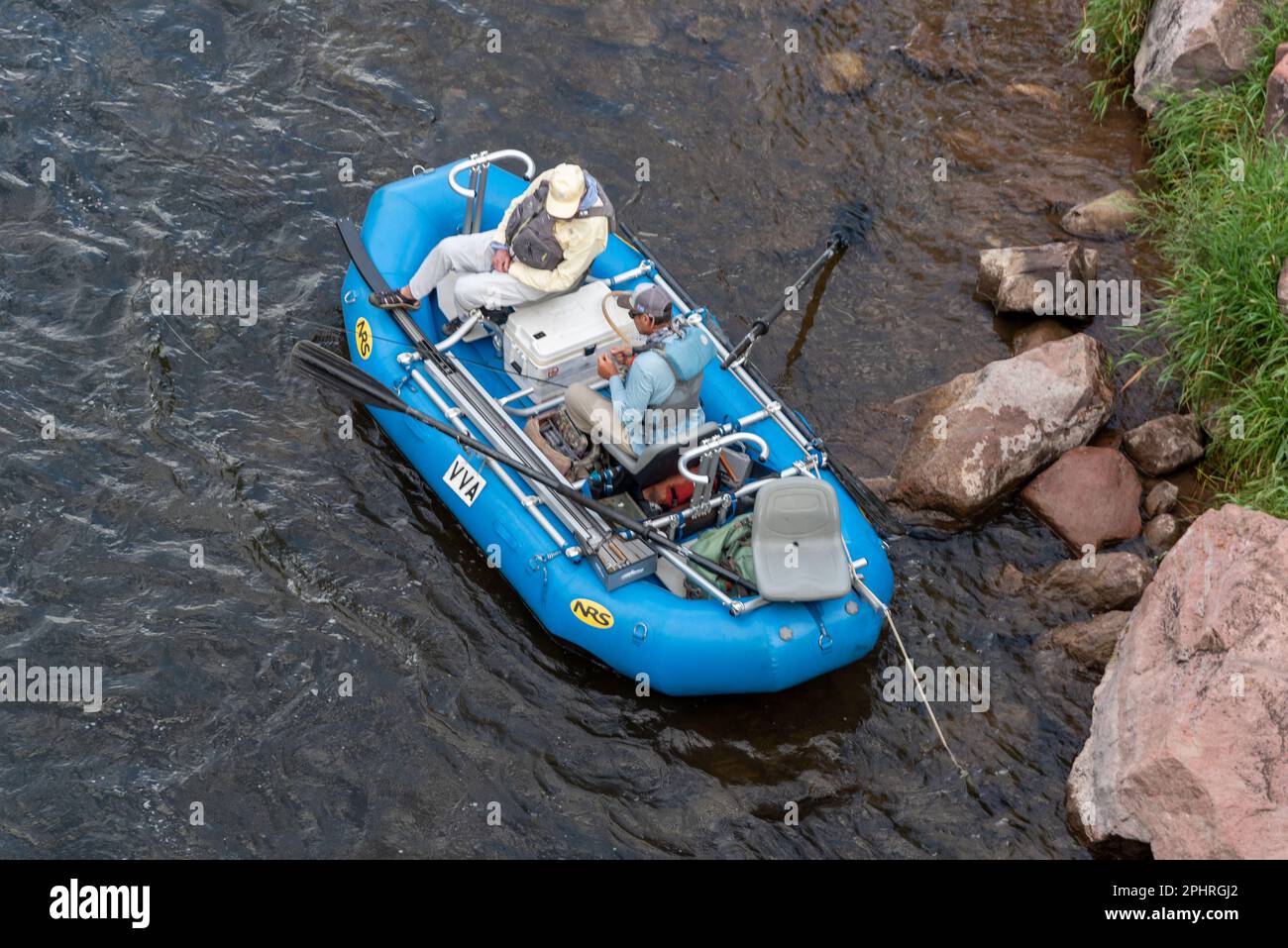 Two men sit in a blue inflatable boat with fishing gear anchored on the
