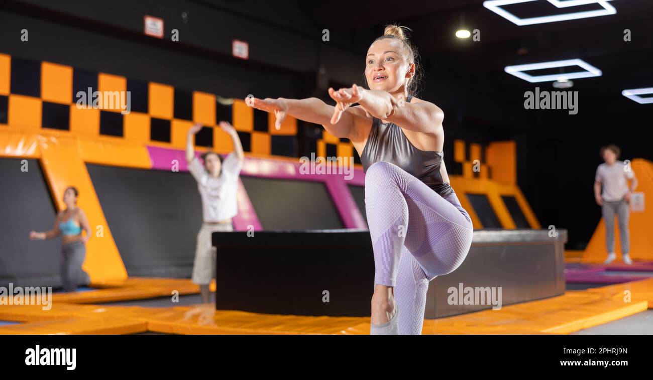 Middle-aged woman in sport clothes doing exercises in trampoline arena ...