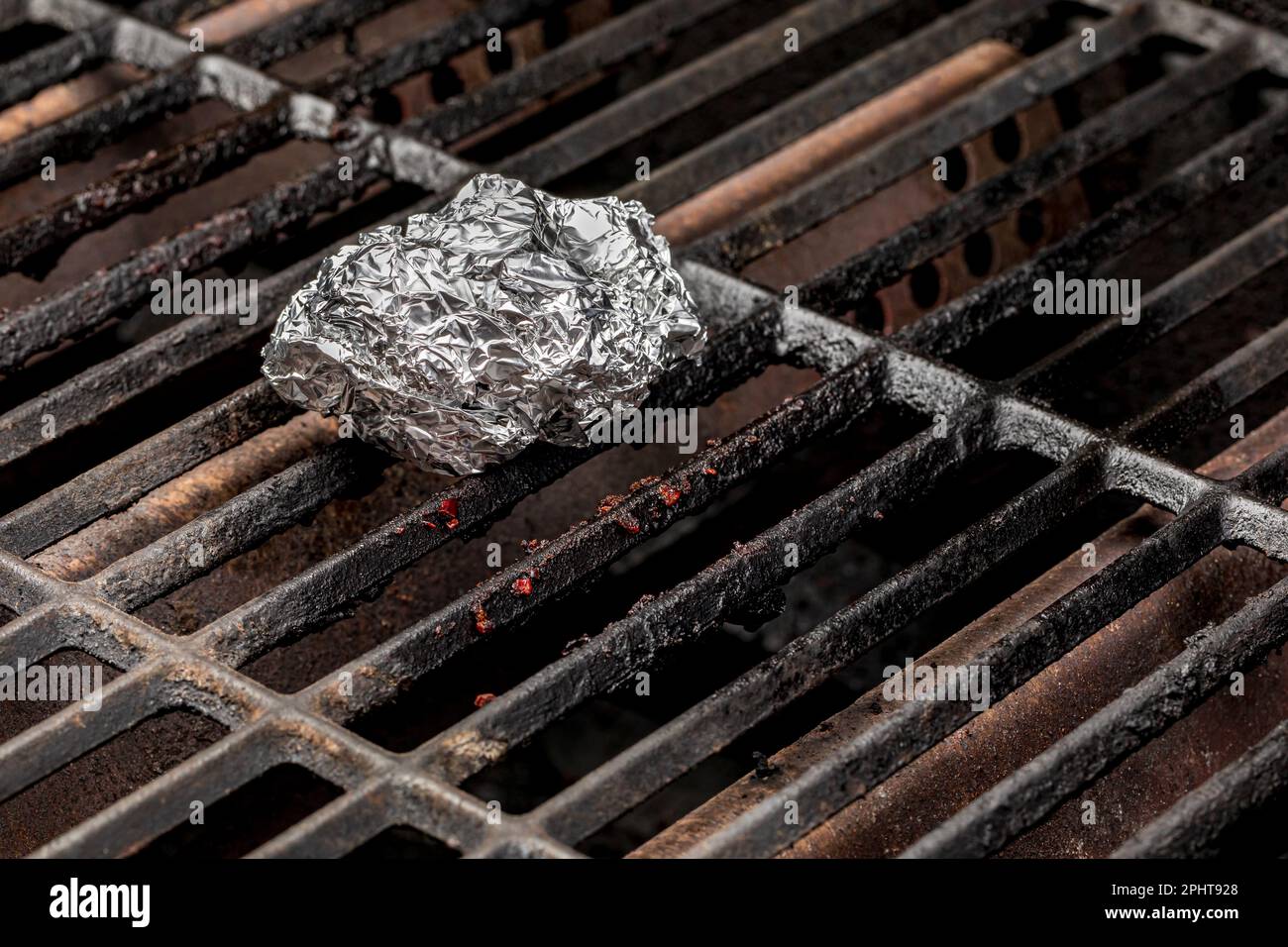 Cleaning burnt food on dirty barbecue grill grates with aluminum foil. Barbeque grilling, cleaning and food safety concept. Stock Photo