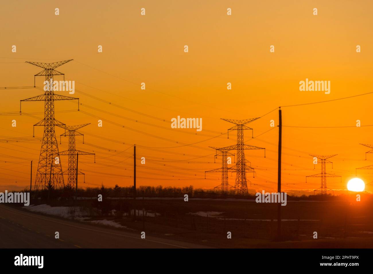 Powerlines and pylons are silhouetted against the glow of the sunset ...