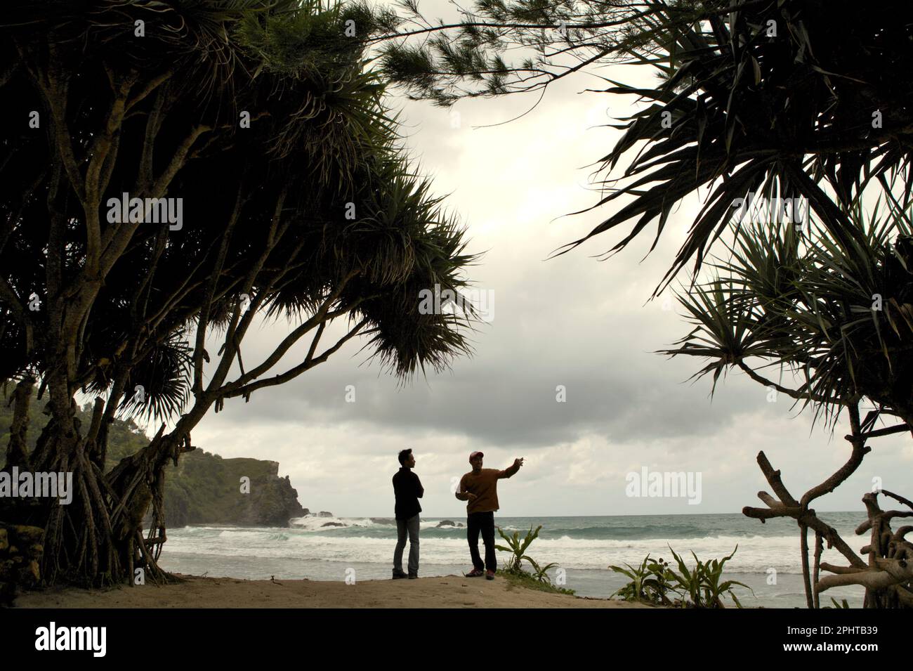 Rock climbers have a conversation as they are standing on sandy beach upon arrival, in a background of a limestone hill and Indian Ocean in a coastal area called Siung Beach, which is administratively located in Duwet, Purwodadi, Tepus, Gunungkidul, Yogyakarta, Indonesia. The beach is one of the popular coastal recreation destinations facing Indian Ocean in the special region of Yogyakarta. For rock climbing enthusiasts, Siung Beach offers more than 200 sport routes that are already established on the face of its limestone hills. Stock Photo