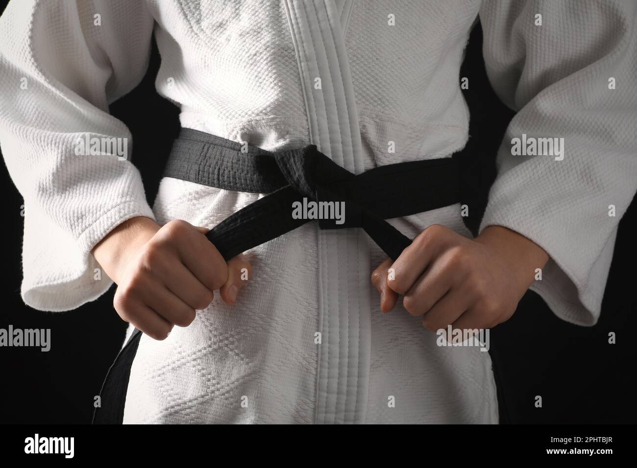 Man in keikogi with black belt on dark background, closeup. Martial arts uniform Stock Photo