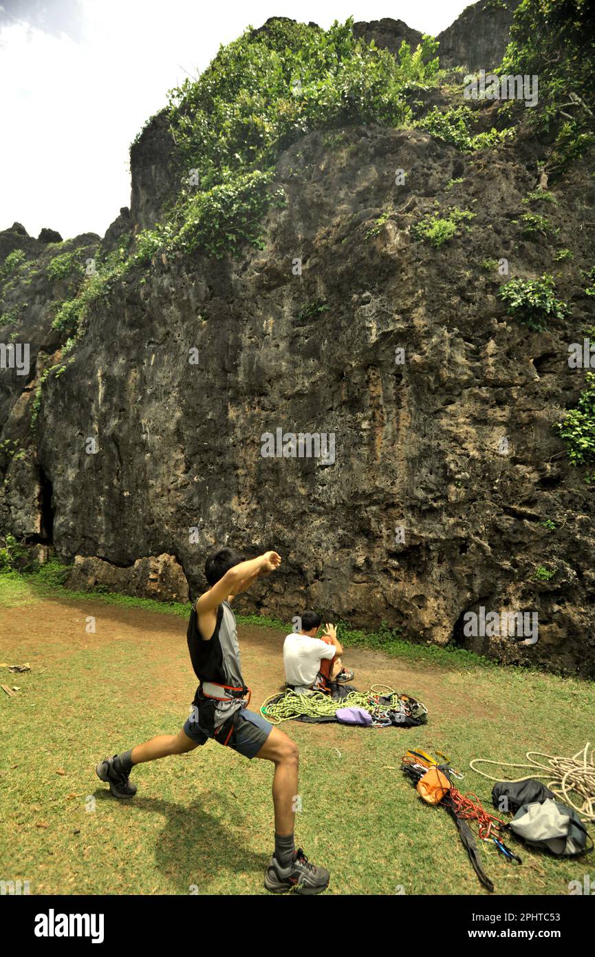 A rock climber stretches as he is getting ready in front of the face of a limestone hill for a sport climbing session in a coastal area called Siung Beach, which is administratively located in Duwet, Purwodadi, Tepus, Gunungkidul, Yogyakarta, Indonesia. The beach is one of the popular coastal recreation destinations facing Indian Ocean in the special region of Yogyakarta. For rock climbing enthusiasts, Siung Beach offers more than 200 sport routes that are already established on its limestone hills. Stock Photo