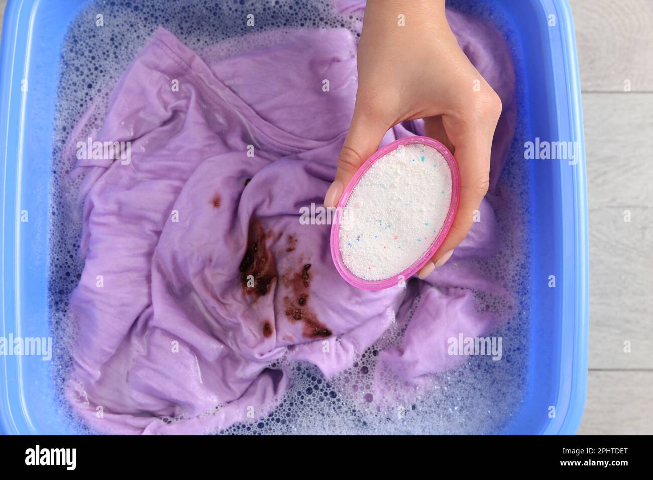 Woman adding powdered detergent into basin with clothes, top view. Hand