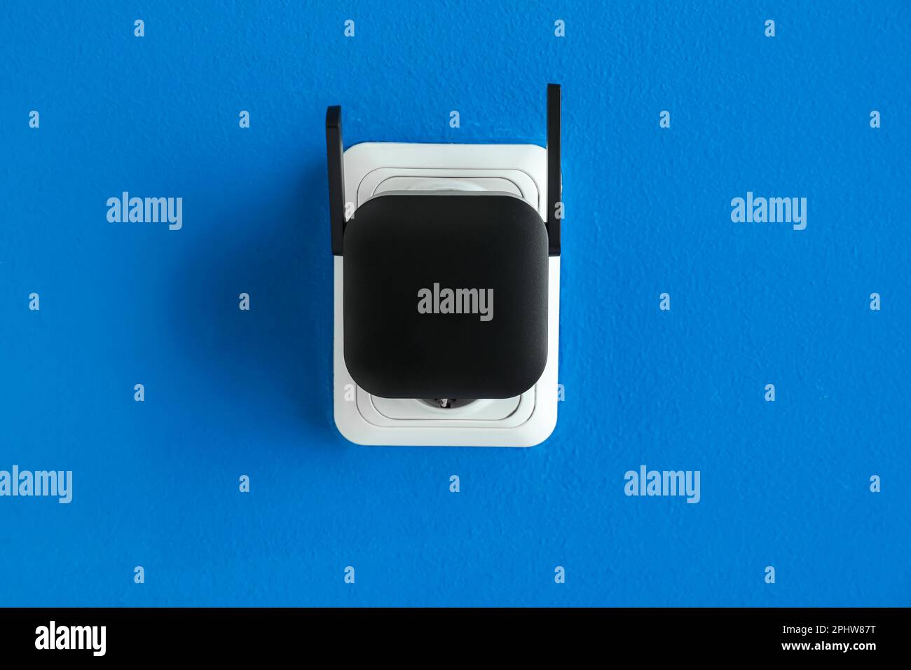 Black WiFi repeater in electric socket on blue wall Stock Photo