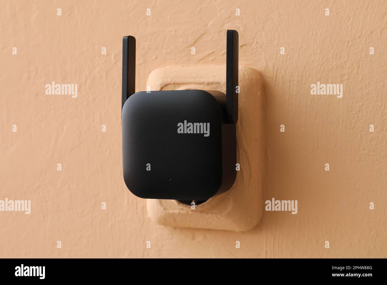 Black WiFi repeater in electric socket on beige wall Stock Photo