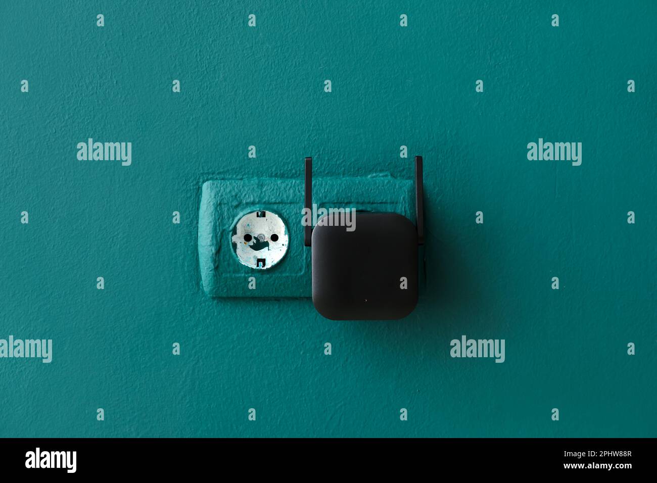 Black WiFi repeater in electric socket on green wall Stock Photo